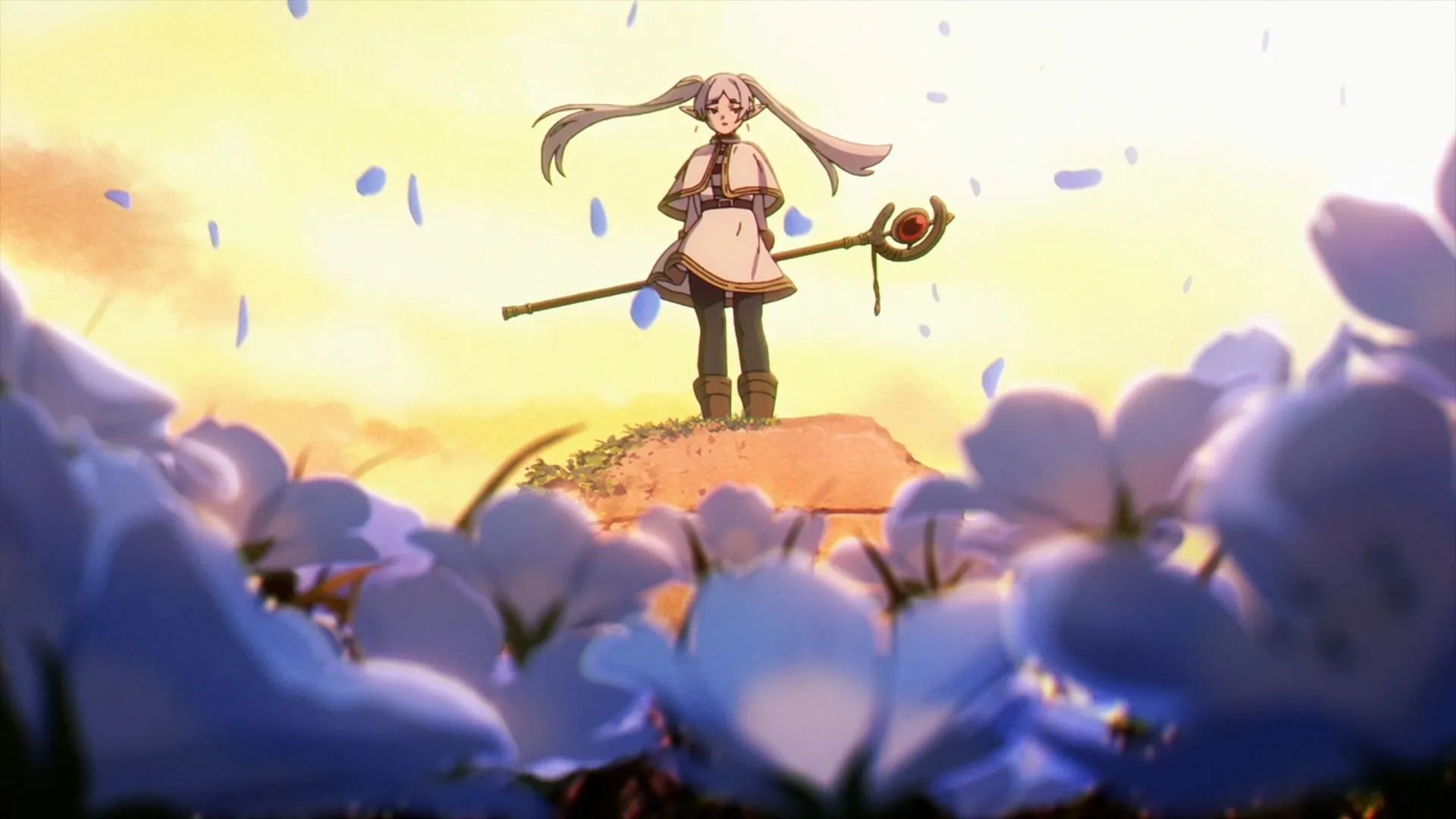 Frieren con su bastón sobre una colina entre flores azules y pétalos al viento (escena de Sousou no Frieren)